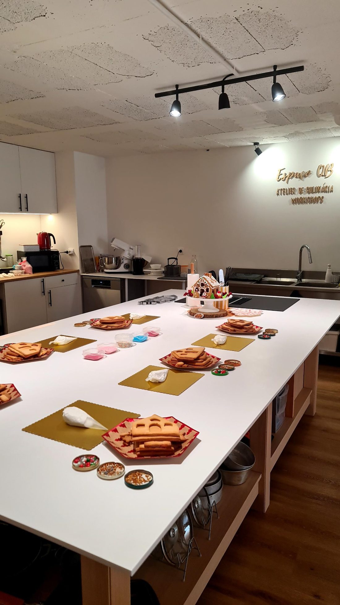 Mesa preparada para o workshop, com as peças de bolacha, mangas de glacé e decorações para cada equipa