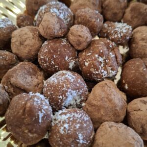 Bolinhas energéticas de aveia e cacau num prato dourado, algumas com coco ralado