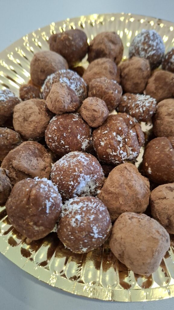 Bolinhas energéticas de aveia e cacau num prato dourado, algumas com coco ralado