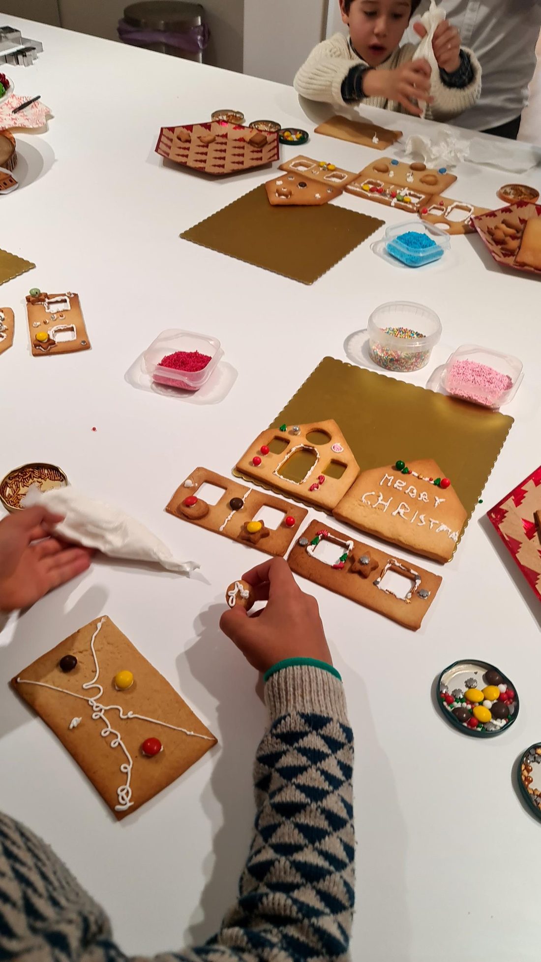 Criança a decorar as peças da casa de bolacha com smarties e glacé