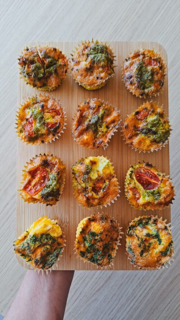 Muffins de ovo na airfryer com tomate cherry, pesto e espinafres numa tábua de madeira